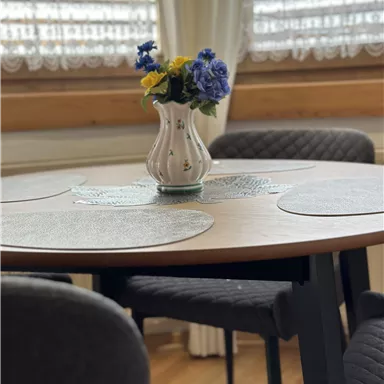 Ein runder Tisch mit einem eleganten Blumenstrauß in einer Vase. Die Atmosphäre ist gemütlich und einladend.