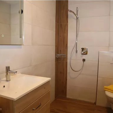 A modern bathroom with a shower, a sink, and a toilet. The walls are bright and the decor is simple and elegant.