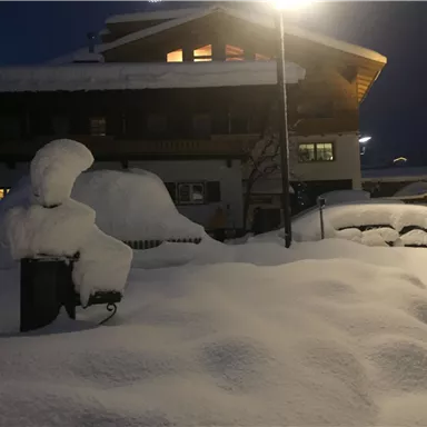 A snowy landscape at night with a illuminated building in the background. The snow is deep and covers the surroundings.