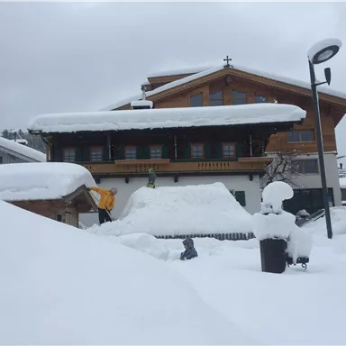 A snowy landscape with a wooden house and thick layers of snow. Fresh snow covers everything under a gray sky.