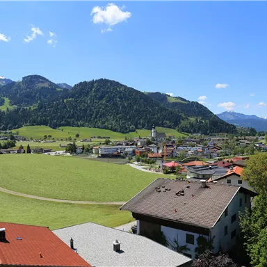A picturesque landscape with green hills and snow-capped mountains in the background. In the foreground, charming houses and a small village can be seen.