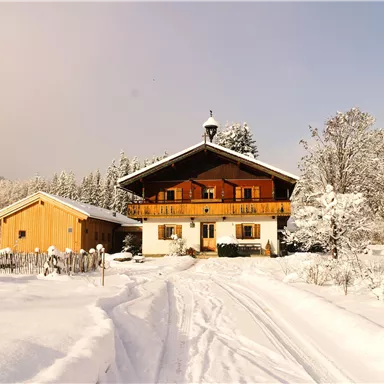 Ein gemütliches Haus im Schnee mit einem großen Balkon. Die Umgebung ist winterlich verschneit und von Bäumen umgeben.