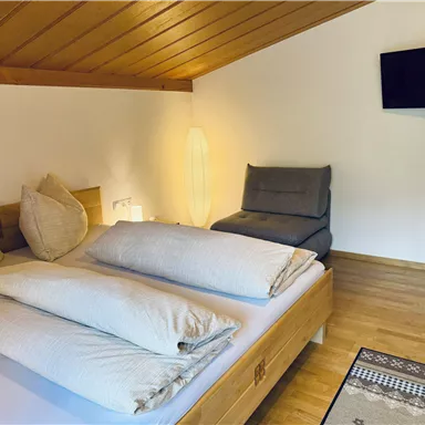 A cozy bedroom with a large bed and two pillows. A TV is mounted on the wall, and there is also a seating area.