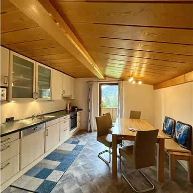 A modern kitchen with a dining area in a bright, friendly space. Large windows offer a view outside and provide plenty of light.