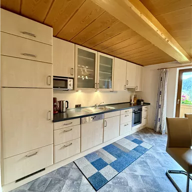 A modern kitchen with bright cabinets and a dark workspace. The floor is decorated with a gray carpet and tiles.