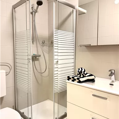A modern bathroom with a glass shower and a white sink. On the sink lies a striped towel and the walls are brightly tiled.