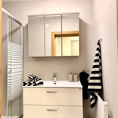 A modern bathroom with a white washbasin and a large mirror. Towels in a black-and-white striped design are hung next to the sink.