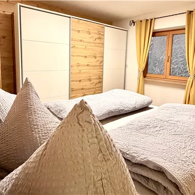 A cozy bedroom with two beds and large pillows. The walls are made of wood, and the window has yellow curtains.