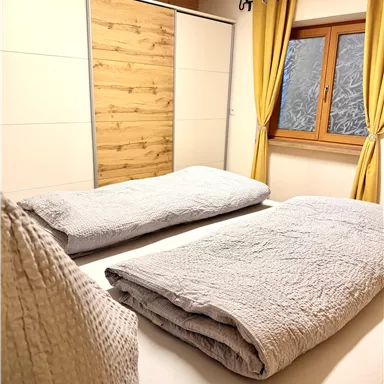 A cozy bedroom with two single beds and a window. The yellow curtains give the room a friendly atmosphere.