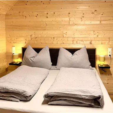 A cozy bedroom with wooden paneling and a large double bed. The bedding is in soft shades of gray, and there is gentle light from bedside lamps.