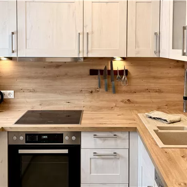 A modern kitchen with wooden paneling and white cabinets. It features cooktops, an oven, and a sink.