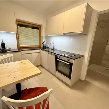 A modern kitchen with bright cabinets and a dining area. There is an oven, a sink, and a window that lets in daylight.