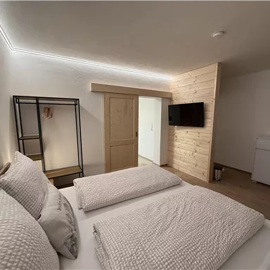 A modern bedroom with two beds and tasteful furnishings. There is a flat-screen TV and harmonious wooden elements.