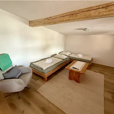 A quiet room with two beds and wooden dishes. A cozy seating area and a carpet complete the subtle ambiance.