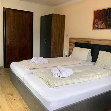 Ein gemütliches Schlafzimmer mit zwei Betten und frischen Handtüchern. Der Raum hat einen schlichten, modernen Stil und viel natürliches Licht.