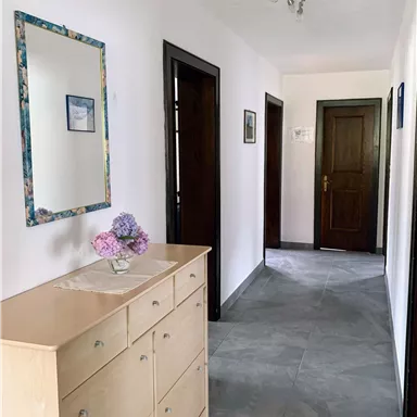 Ein heller Flur mit einem Holzschrank und einem Spiegel an der Wand. Es gibt mehrere Türen, die zu anderen Räumen führen.