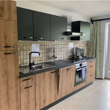 Eine moderne Küche mit Holzfronten und schwarzen Schränken. Sie ist hell und hat ein Fenster mit Blick nach draußen.