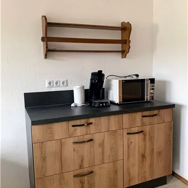Eine moderne Küche mit Holzschränken und einer Arbeitsplatte. Auf der Theke sind eine Kaffeemaschine und eine Mikrowelle sichtbar.