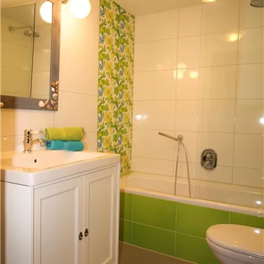 A modern bathroom with a bathtub and a toilet. The walls are decorated with white tiles and green accents.