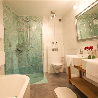 A modern bathroom with a transparent shower cabin and a beautiful bathtub. The walls are designed with light tiles and a blue pattern.