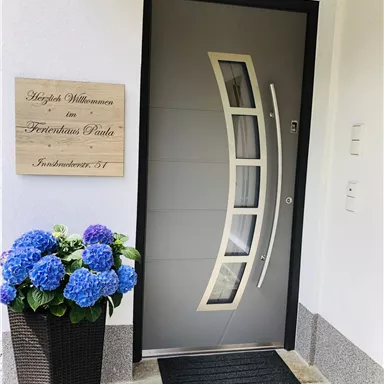 Eine moderne Haustür mit einer eleganten Form und einem dekorativen Namensschild. Neben der Tür steht ein Blumentopf mit blauen Hortensien.