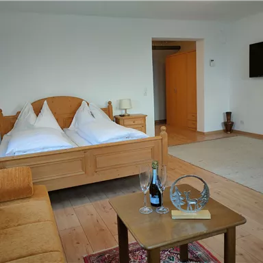 A cozy bedroom with a large double bed and wooden furniture. In the foreground, there are champagne glasses and a bottle of champagne on a table.