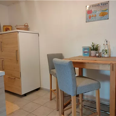 A modern kitchen with a small wooden tray and chairs. In the background, there is a refrigerator and a plant on the table.