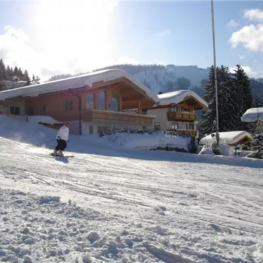A snowy landscape with skiers and chalets. The sky is blue and the sun is shining.