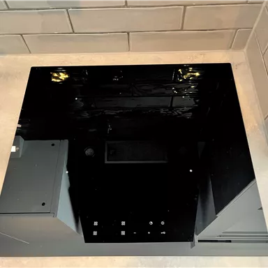 A modern black cooktop on a gray countertop. In the background, gray tiles are visible.