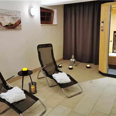 A relaxing wellness area with two loungers and soft lighting. In the background, a sauna can be seen that invites rest and relaxation.