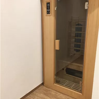 A modern sauna made of wood with a glass door. The floor is tiled and the walls are plain white.