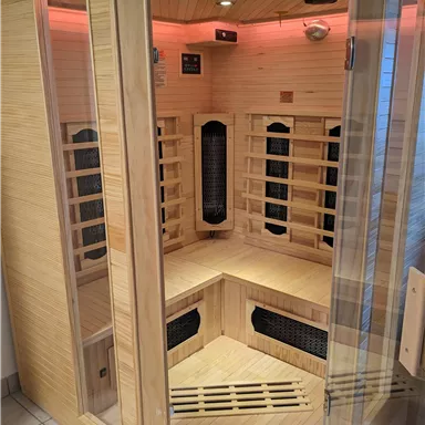 Eine Infrarotsauna aus Holz mit Glaswänden. Sie ist hell beleuchtet und verfügt über mehrere Heizstrahler.