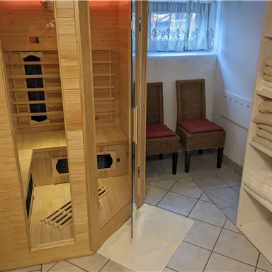 Ein ruhiger Wellnessbereich mit einer Sauna aus Holz und zwei Stühlen. Auf der rechten Seite befinden sich gefaltete Handtücher.