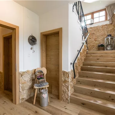 Ein heller Flur mit Holzfußboden und Wänden aus Stein. Eine Treppe führt nach oben, und eine gemütliche Dekoration befindet sich in der Ecke.