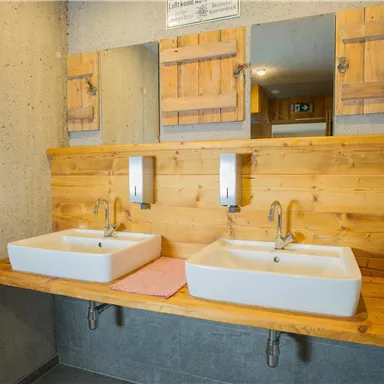 Zwei moderne Waschbecken mit Holzverkleidung in einem Badezimmer. Über den Waschbecken hängen Spiegel und daneben sind Holzschränke.
