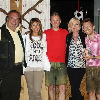 Eine Gruppe von fünf Personen in traditioneller bayerischer Tracht in einem gemütlichen Restaurant. Sie lächeln und posieren für ein Foto.