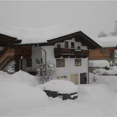 A house surrounded by a lot of snow. The sky is gray and there are many snow-covered trees.