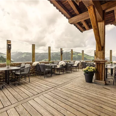 Eine Terrasse mit Holzfußboden und stilvollen Möbeln bietet einen Blick auf die Berge. Der Himmel ist bewölkt, was eine gemütliche Atmosphäre schafft.