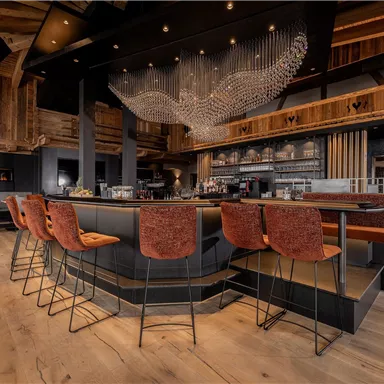 Eine moderne Bar mit stilvollen Stühlen und einer eleganten Holzdecke. Das Ambiente ist gemütlich und einladend.