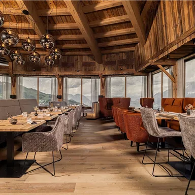 Ein modernes Restaurant mit Holzvertäfelung und großen Fenstern. Die Tische sind elegant gedeckt und bieten einen Blick auf die umliegende Landschaft.