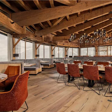 Ein modernes Restaurant mit Holzdecke und großen Fenstern. Die Tische sind elegant gedeckt und die Stühle sind orangefarben.