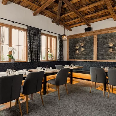 Ein modernes Restaurant mit Holzbalkendecke und gemütlichen Sitzbereichen. Die elegante Einrichtung zeigt einen schönen Kontrast zwischen Steinwänden und weichen Stoffen.