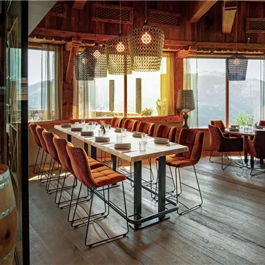Ein stilvolles Restaurant mit Holzelementen und großem Fensterblick auf die Berge. Die Tische sind elegant gedeckt und die Stühle bieten einen komfortablen Sitzplatz.