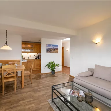 Ein helles Wohnzimmer mit einem gemütlichen Sofa und einem Esstisch. Die modernen Möbel und Holzfußböden schaffen eine einladende Atmosphäre.