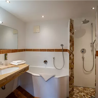 Ein modernes Badezimmer mit einer Badewanne und einer Dusche. Die Wände sind hell und die Einrichtung ist schlicht und elegant.