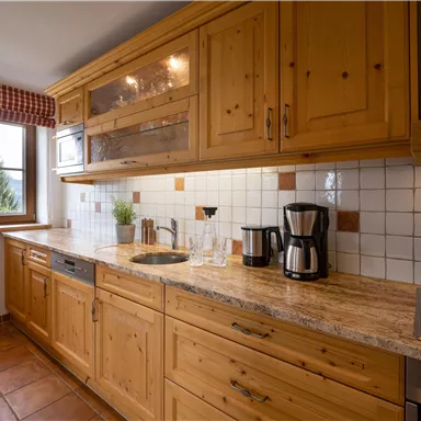 Eine gemütliche Küche mit Holzschränken und einer Granitarbeitsplatte. Auf dem Tisch stehen Gläser und eine Kaffeemaschine.