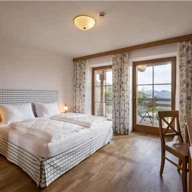 Ein modernes Schlafzimmer mit einem Doppelbett und Holzfußboden. Große Fenster bieten einen Blick auf die Natur.