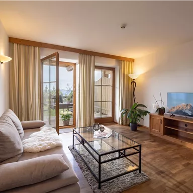 Ein gemütliches Wohnzimmer mit einem hellen Sofa und einem eleganten Couchtisch. Große Fenster bringen viel Tageslicht und einen schönen Ausblick ins Freie.