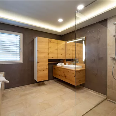 Ein modernes Badezimmer mit einer Dusche und einem eleganten Holzmöbel. Die Wände sind hell und die Beleuchtung sorgt für eine angenehme Atmosphäre.