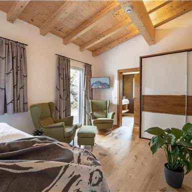 Ein gemütliches Zimmer mit Holzdecke und zwei bequemen Sesseln. Große Fenster bieten einen Blick auf die Natur, und eine Pflanze sorgt für einen frischen Akzent.